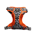 Load image into Gallery viewer, A black and white patterned dog harness with bright orange mesh lining and trim, displayed on a dark reflective surface against a solid beige background.