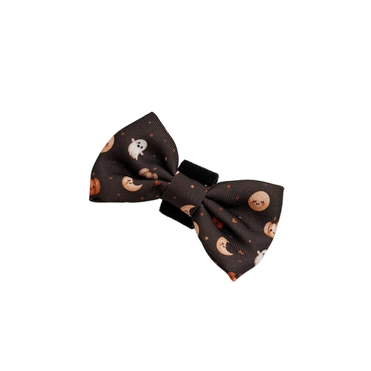 A dark brown fabric hair bow with a cute Halloween print of smiling pumpkins, crescent moons, and white ghosts,