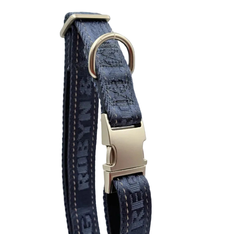 A close-up of a dark blue patterned dog collar with a silver-tone metal buckle and D-ring