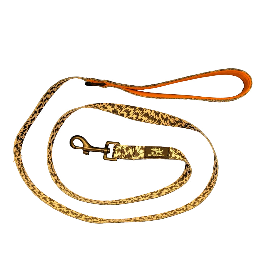 A dog leash with a white and black pattern, a bright orange inner lining, and a black metal clasp